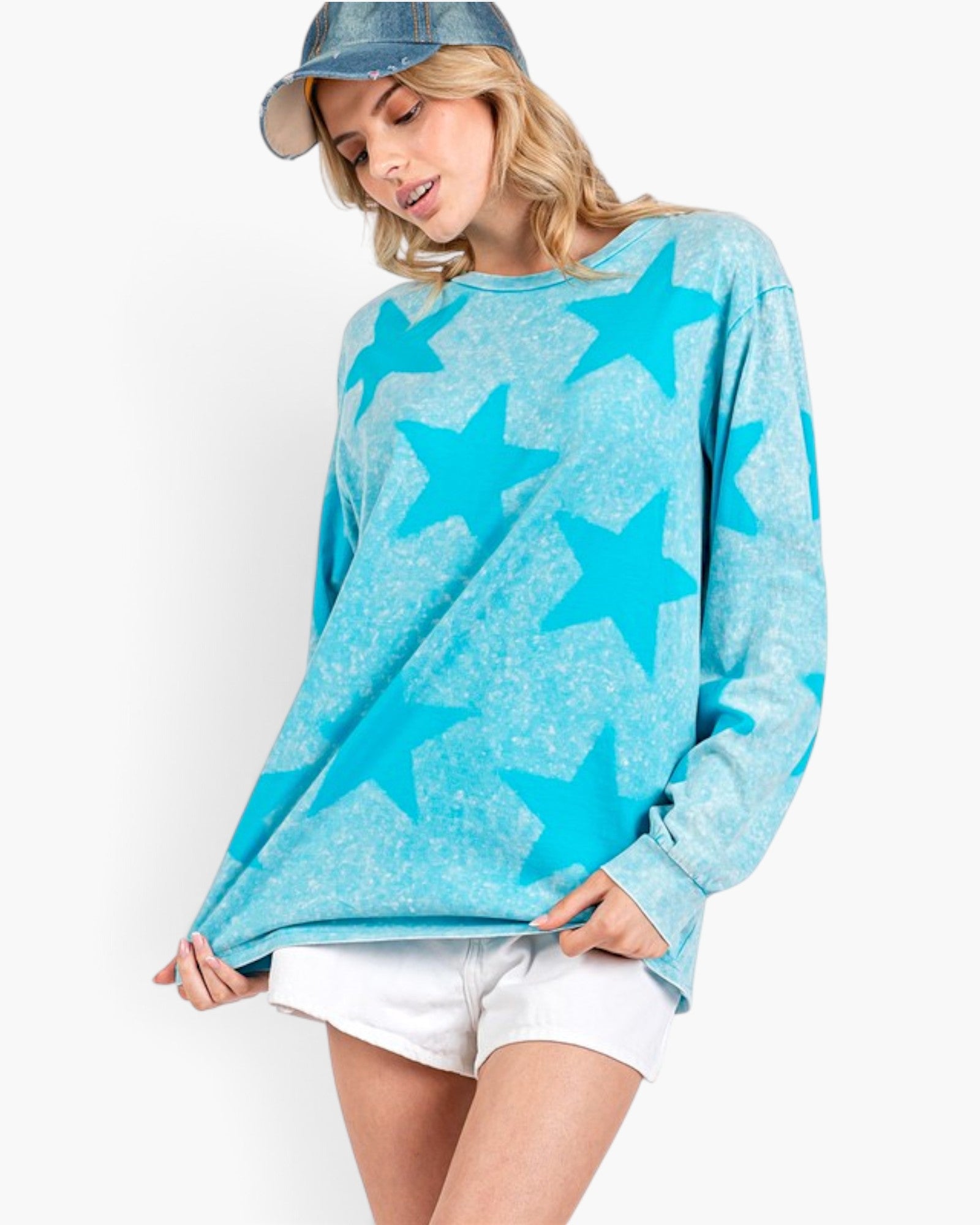 A woman wearing a light blue long-sleeve crewneck sweatshirt with a darker blue star pattern, paired with white shorts and a denim cap, against a plain white background.