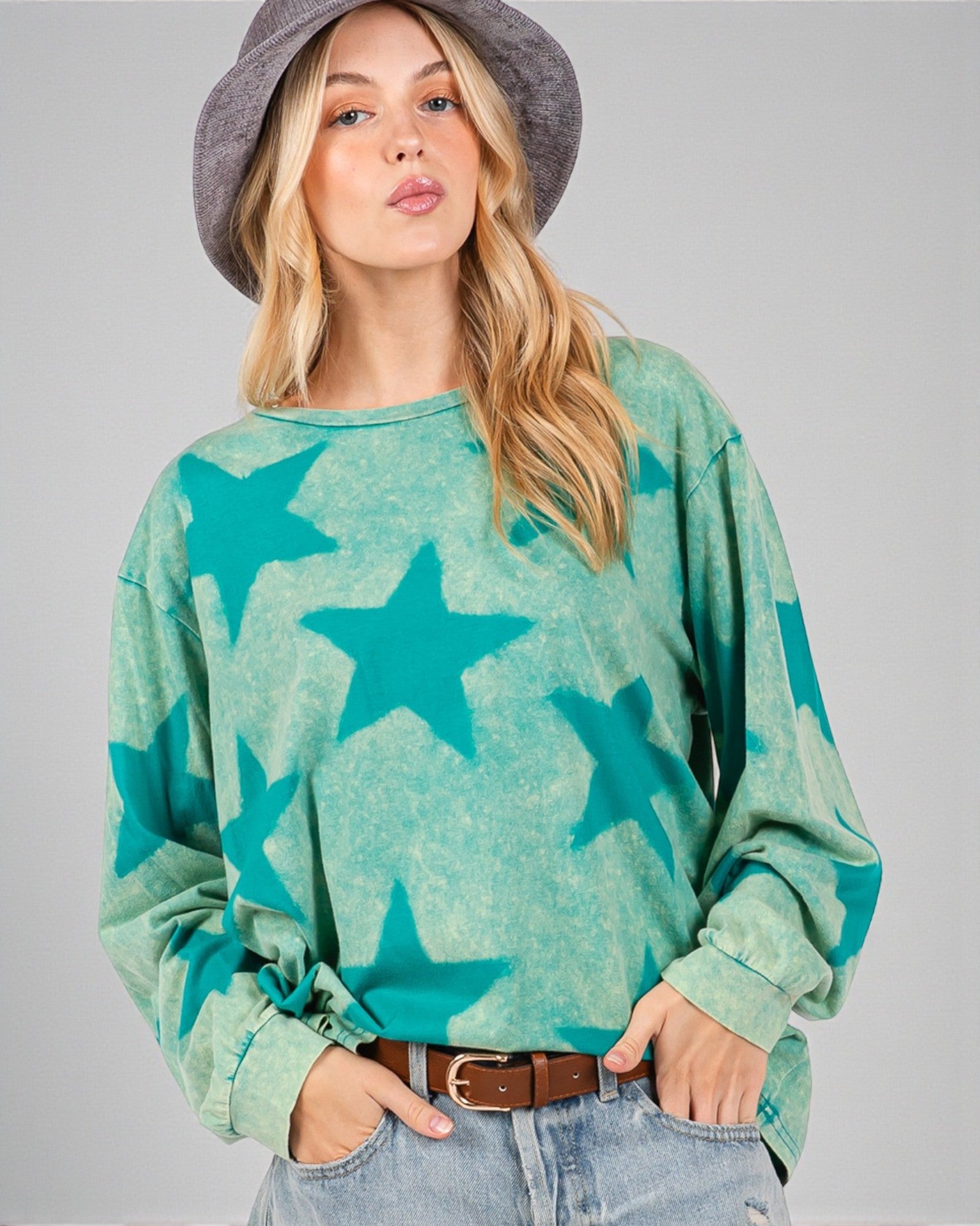 Woman wearing a green sweater with star patterns and a gray hat on a gray background