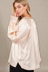 Woman wearing a beige satin blouse against a neutral background
