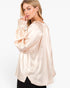 A woman wearing a light peach satin blouse with voluminous long sleeves and a high-low hem, photographed against a plain white studio background.