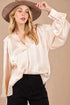 Woman wearing a beige satin blouse and brown hat against a beige background