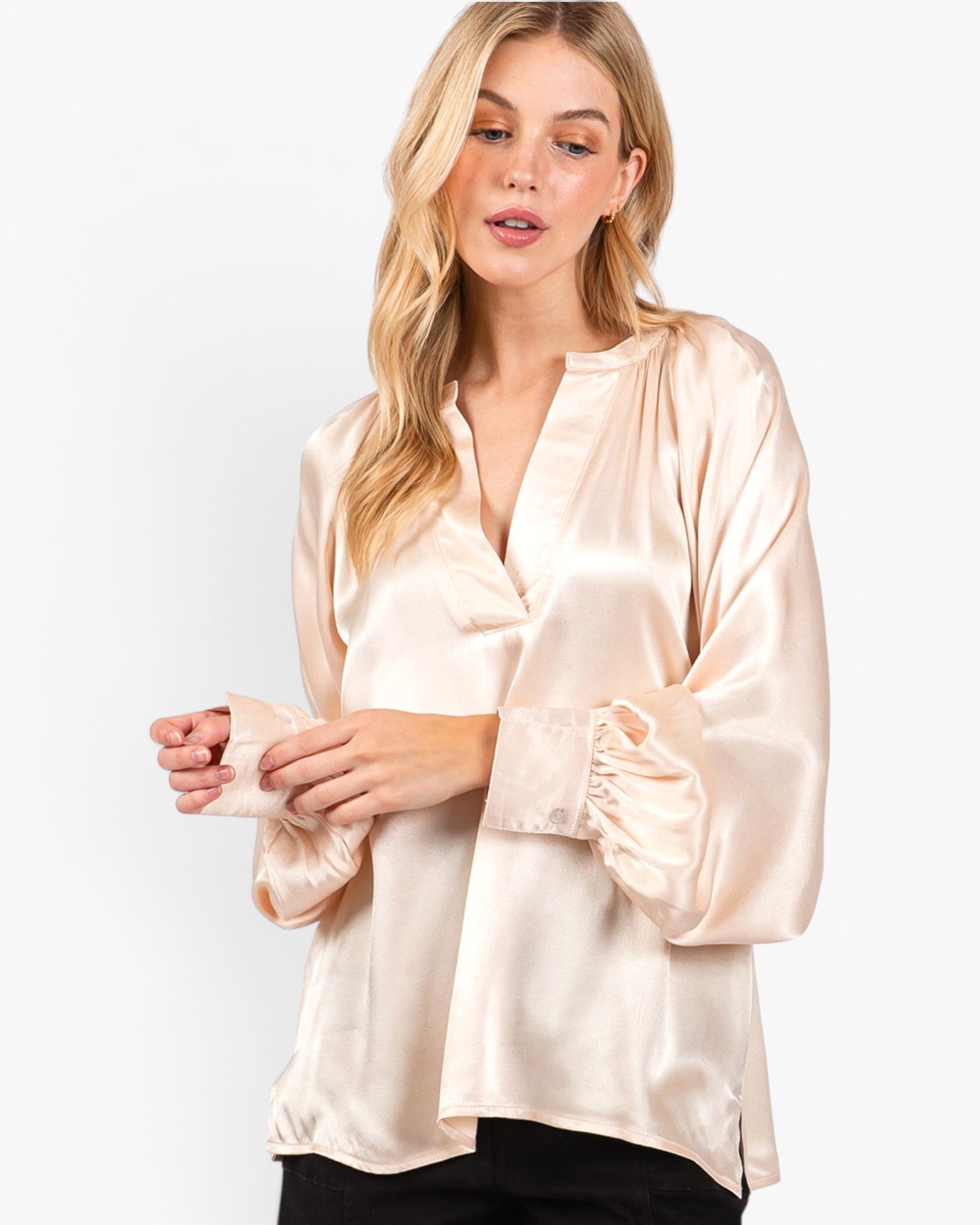 A woman wearing a light beige satin blouse with a split neckline, gathered cuffs, and a loose fit, paired with black pants, against a plain white background.