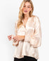 A woman wearing a light beige satin blouse with a split neckline, gathered cuffs, and a loose fit, paired with black pants, against a plain white background.