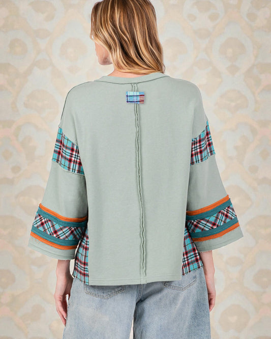 Person wearing a light green top with plaid sleeves against a beige patterned background