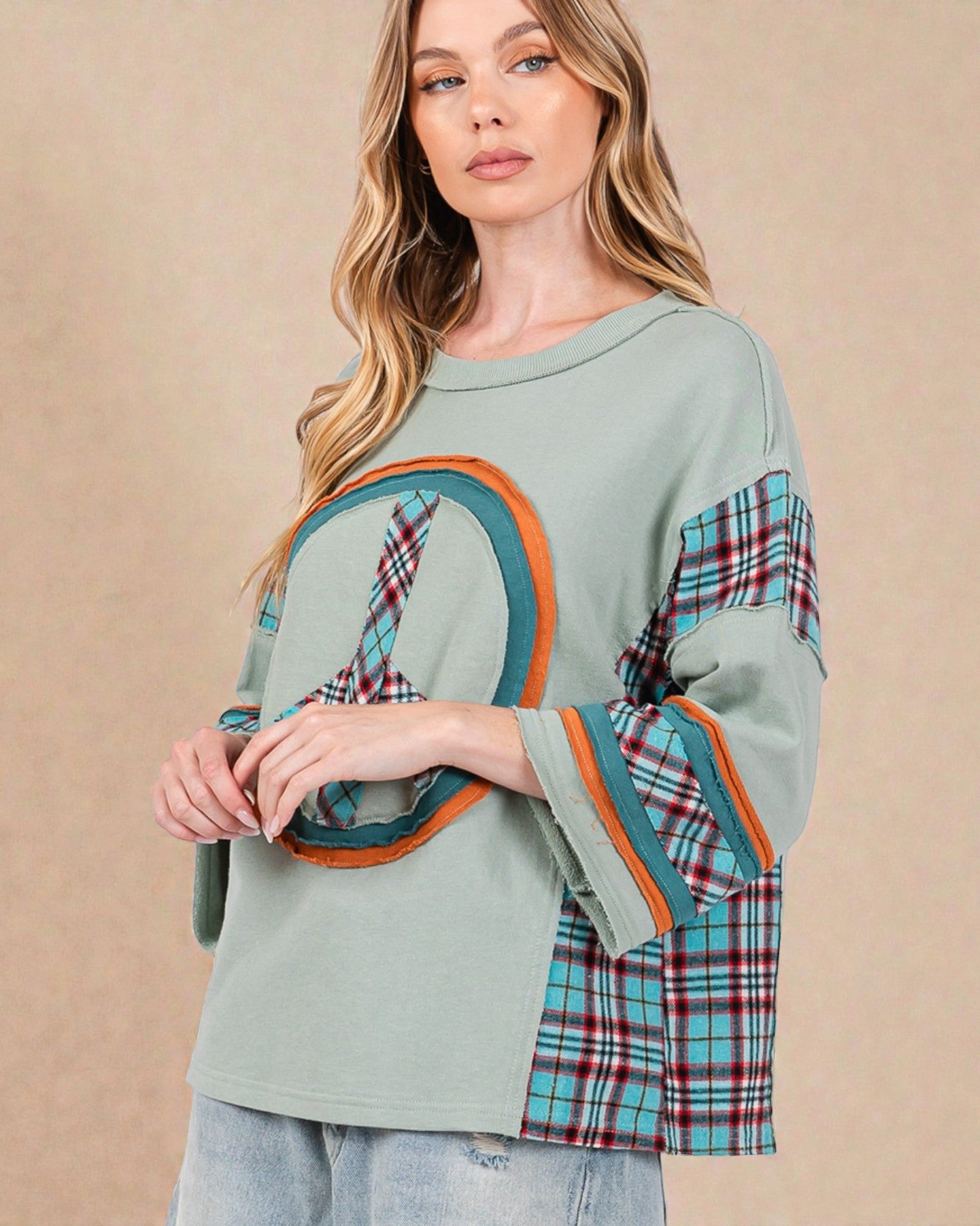 Woman wearing a green sweater with plaid sleeves against a beige background