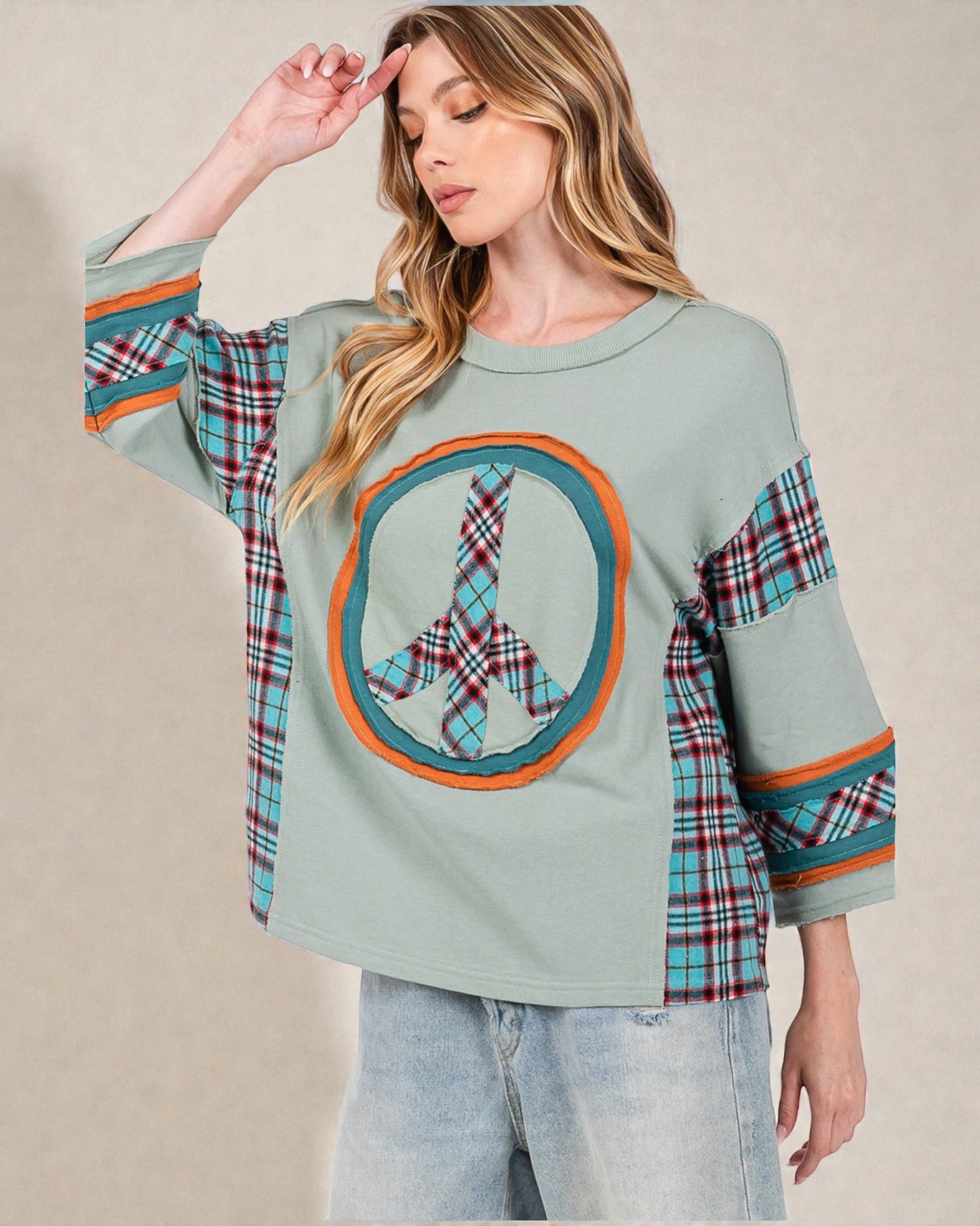 Woman wearing a light green sweater with plaid sleeves and a circular design on a beige background