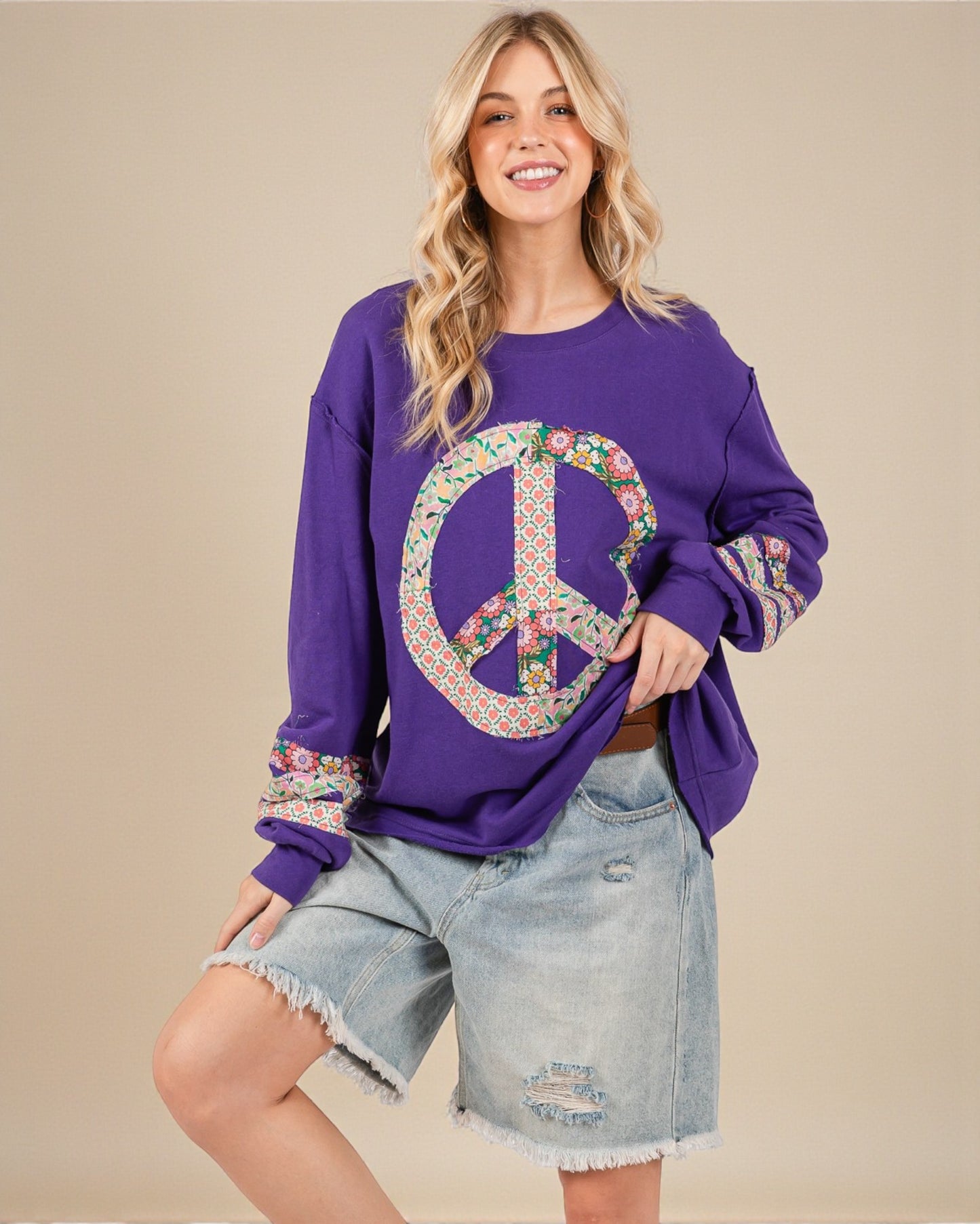 Woman wearing a purple sweatshirt with a peace symbol design on a beige background