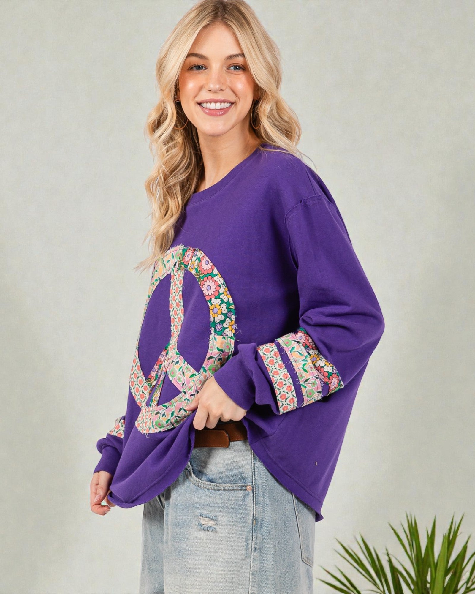 Woman wearing a purple sweatshirt with floral peace symbol design on a plain background