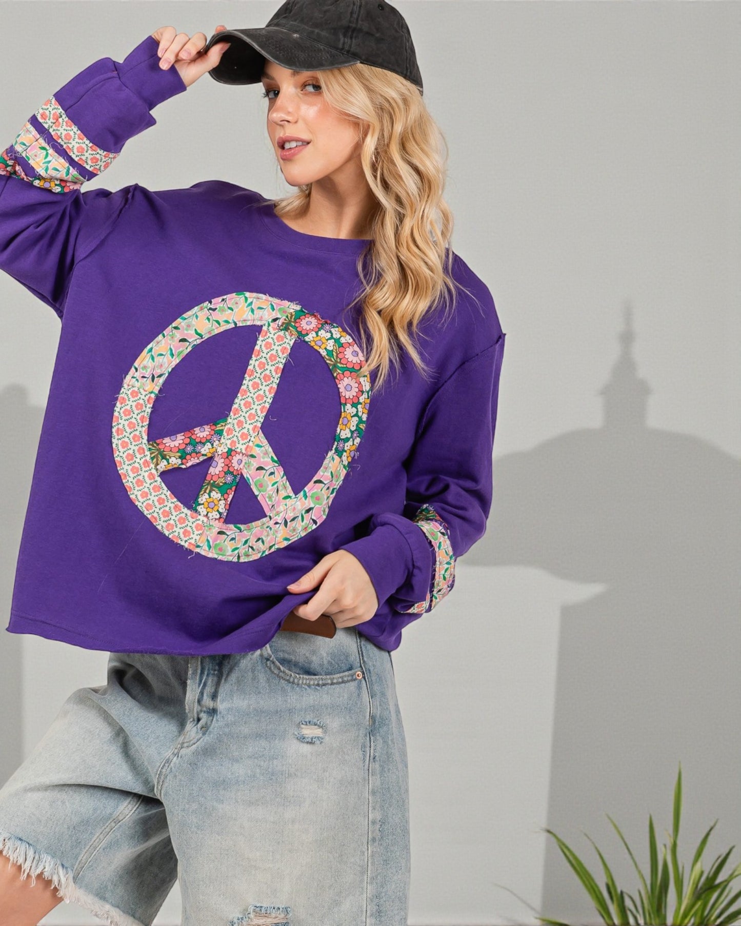 Woman wearing a purple sweatshirt with a peace symbol design, standing against a gray background.
