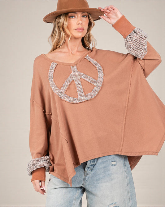 Woman wearing a brown sweatshirt with a peace symbol design, holding a brown hat.