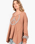 A woman wearing a loose, long-sleeve taupe-brown top with a peace sign cutout embellished with silver rhinestones, paired with light blue jeans, against a plain white background.