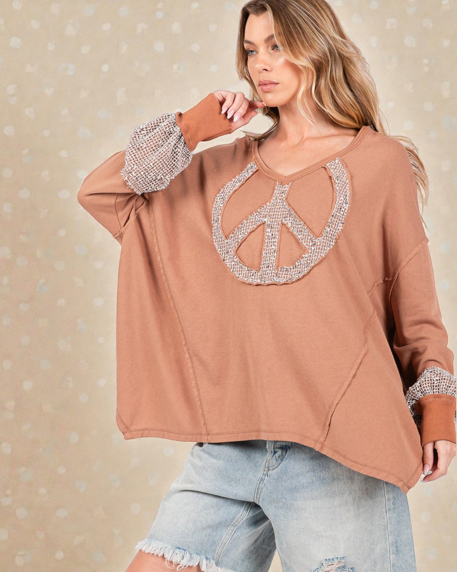 Woman wearing a brown sweatshirt with a peace symbol design on a beige background