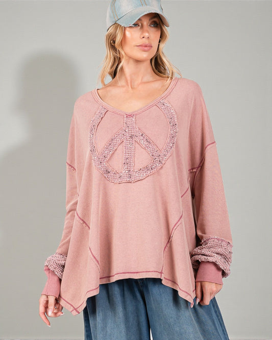 Woman wearing a pink long-sleeve top with a peace sign design on a gray background