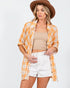 Woman wearing a yellow plaid shirt, beige top, white shorts, and brown hat on a white background