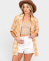 Woman wearing a yellow plaid shirt, beige top, white shorts, and brown hat on a light gray background