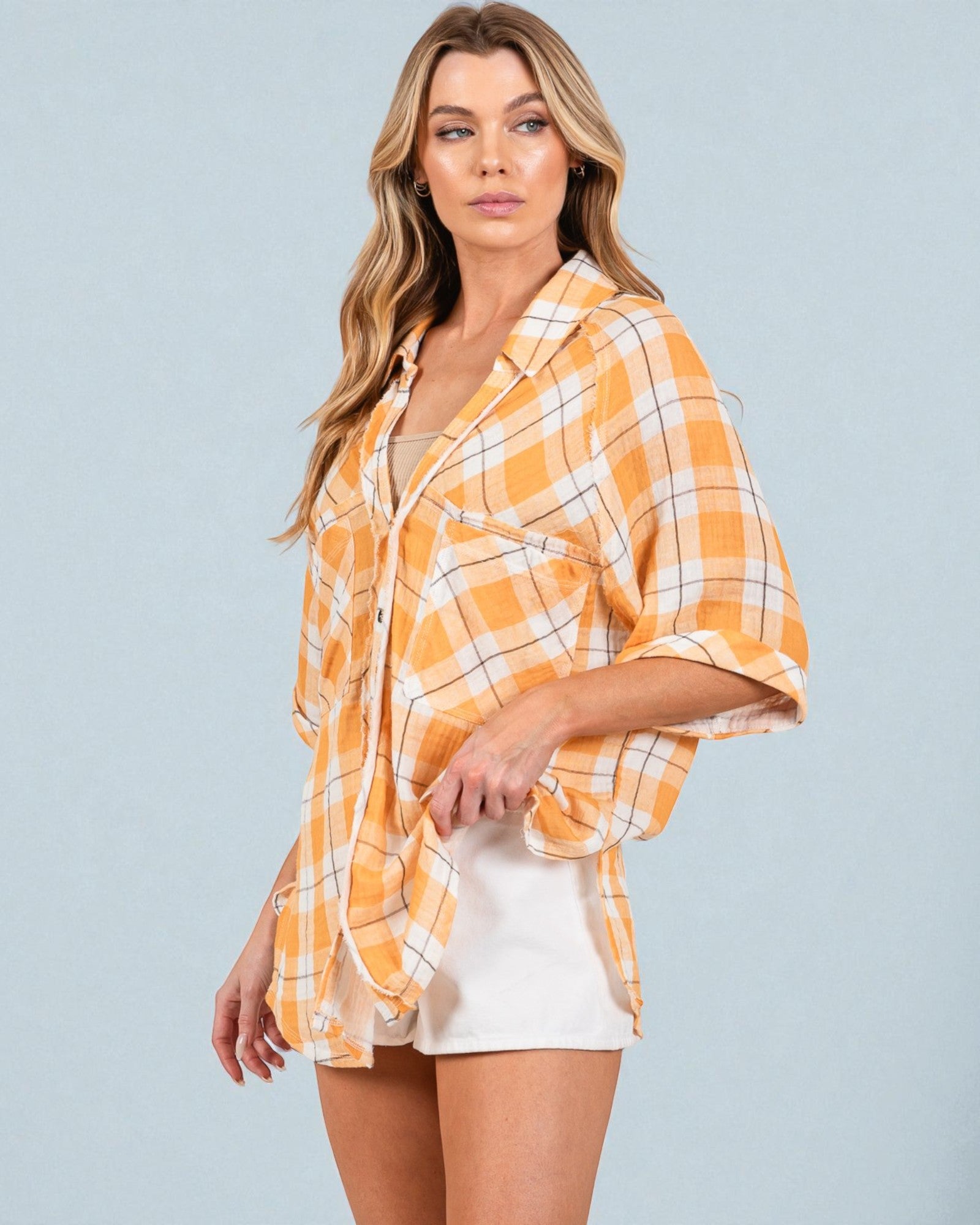 Woman wearing a yellow plaid shirt over a white top with beige shorts on a gray background