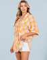 Woman wearing a yellow plaid shirt over a white top with beige shorts on a gray background