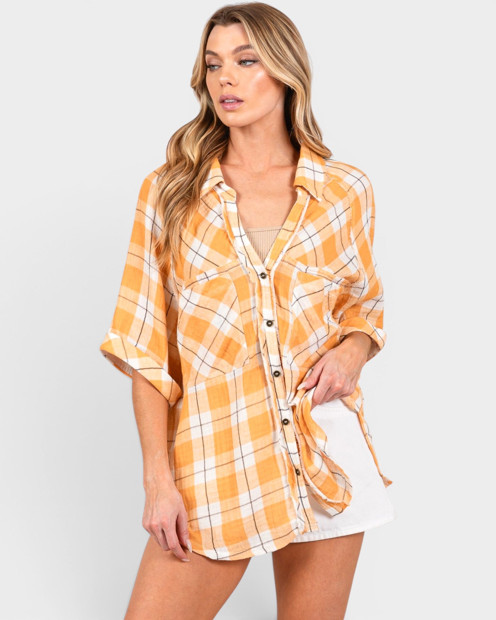 Woman wearing a yellow plaid shirt over a white top and shorts on a light gray background