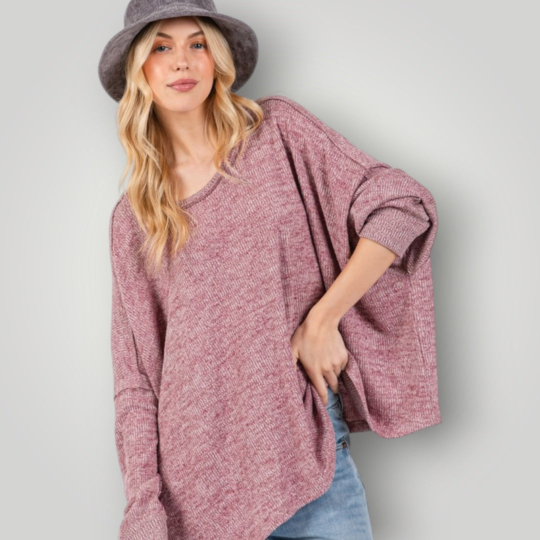 Woman wearing a loose-fitting pink sweater and a gray hat against a plain background