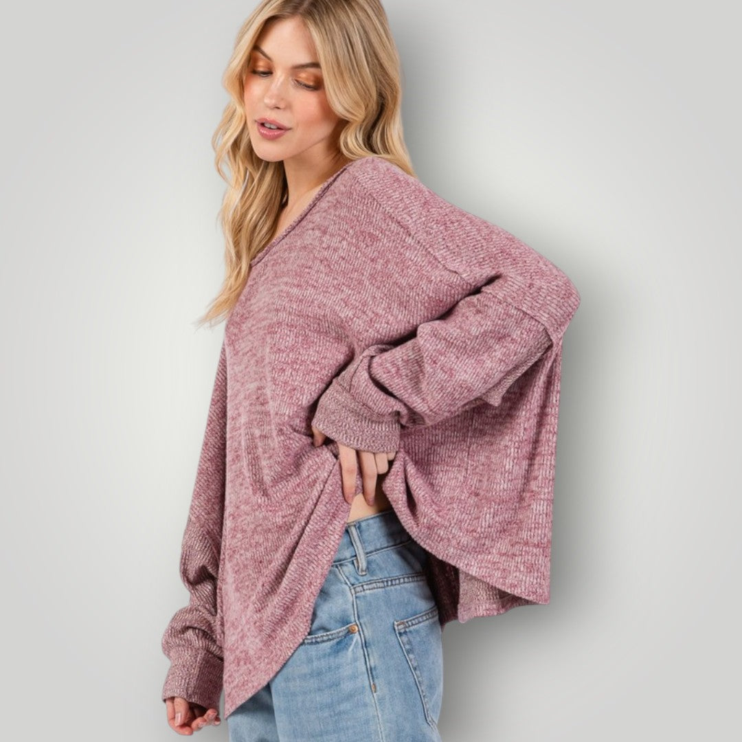 Woman wearing a pink sweater and blue jeans against a light gray background