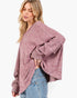 A woman wearing a loose, heathered dusty rose knit sweater with wide sleeves and light blue jeans, photographed against a clean white background.