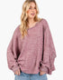 A woman wearing a loose, oversized knit sweater in a heathered dusty rose color, paired with blue jeans, against a plain white background.