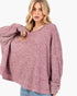 A woman wearing a loose, oversized knit sweater in a heathered dusty rose color, paired with light blue jeans, against a plain white background.