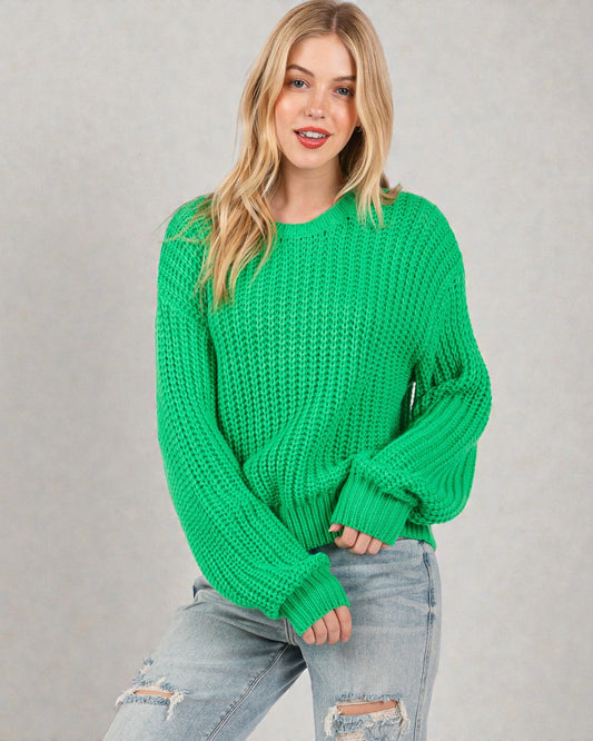 Woman wearing a green chunky knit sweater against a plain background