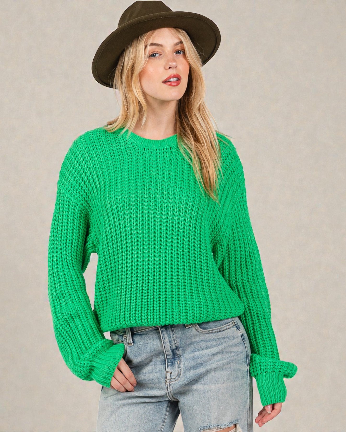 Woman wearing a green knitted sweater and brown hat against a beige background