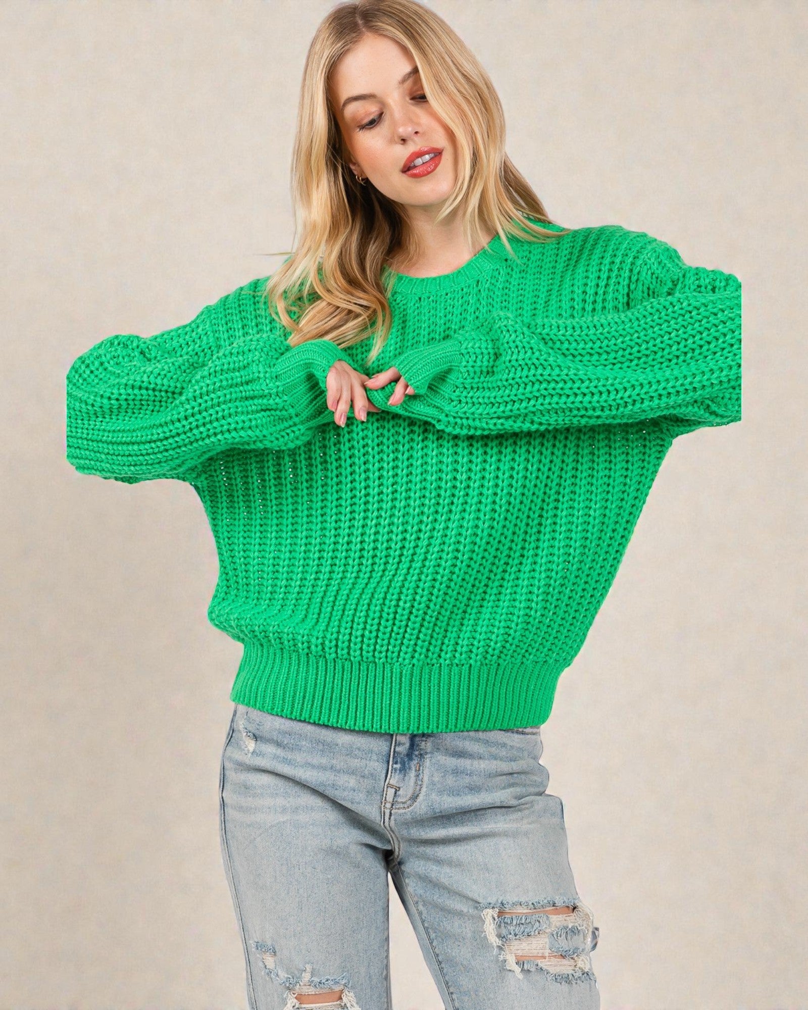 Woman wearing a green knitted sweater and light blue jeans against a beige background