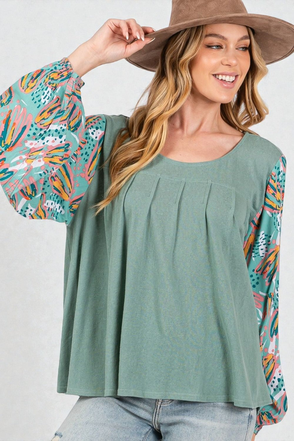 Woman wearing a green top with colorful sleeves and a brown hat against a white background