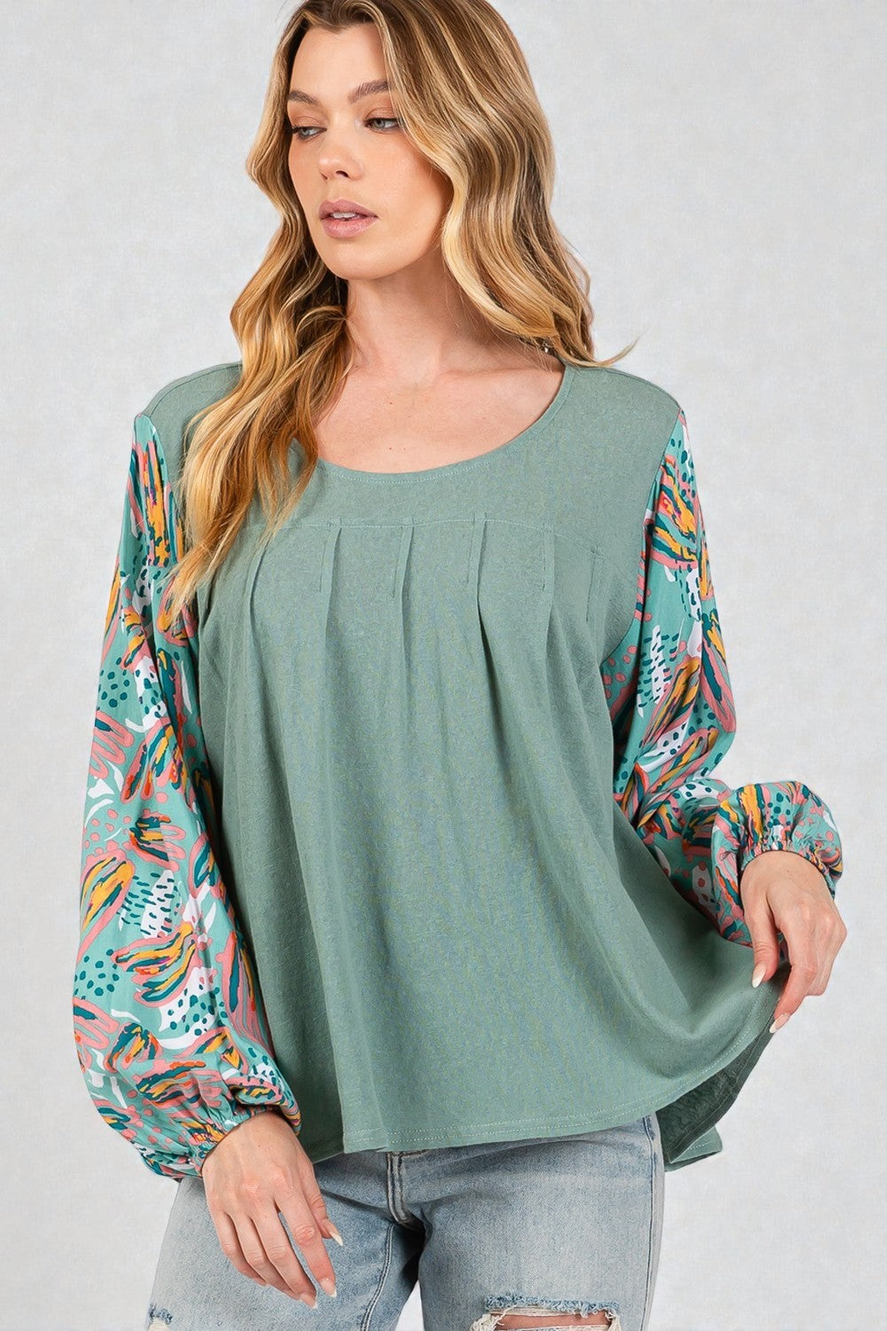 Woman wearing a green top with colorful sleeves on a plain background