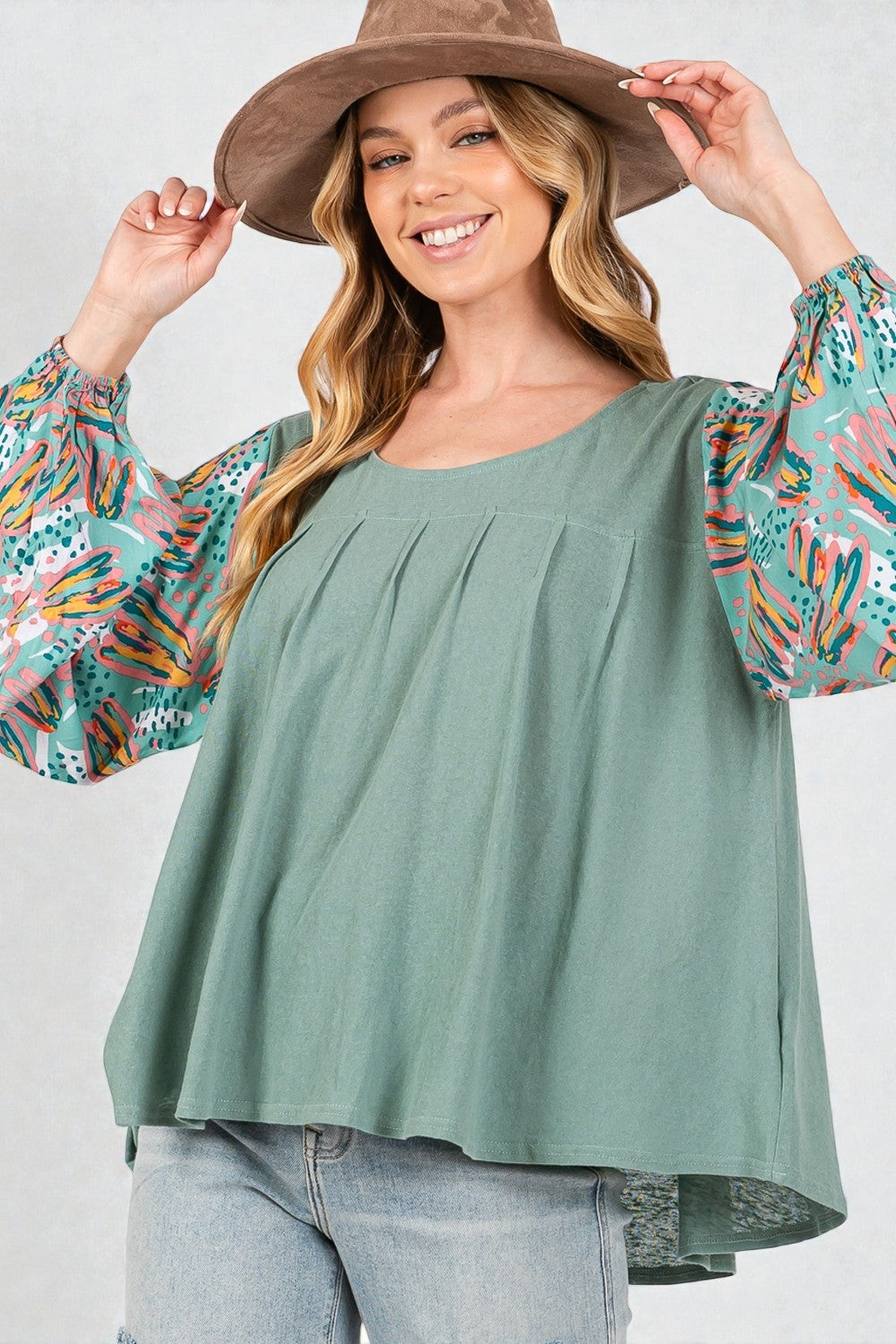 Woman wearing a green top with colorful sleeves and a brown hat on a white background