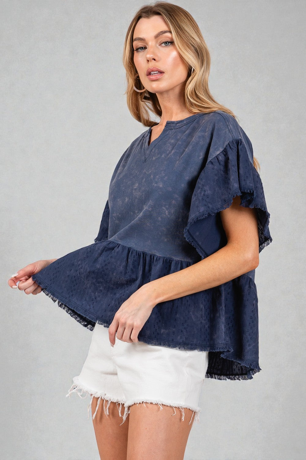 Woman wearing a blue top with ruffled sleeves on a gray background