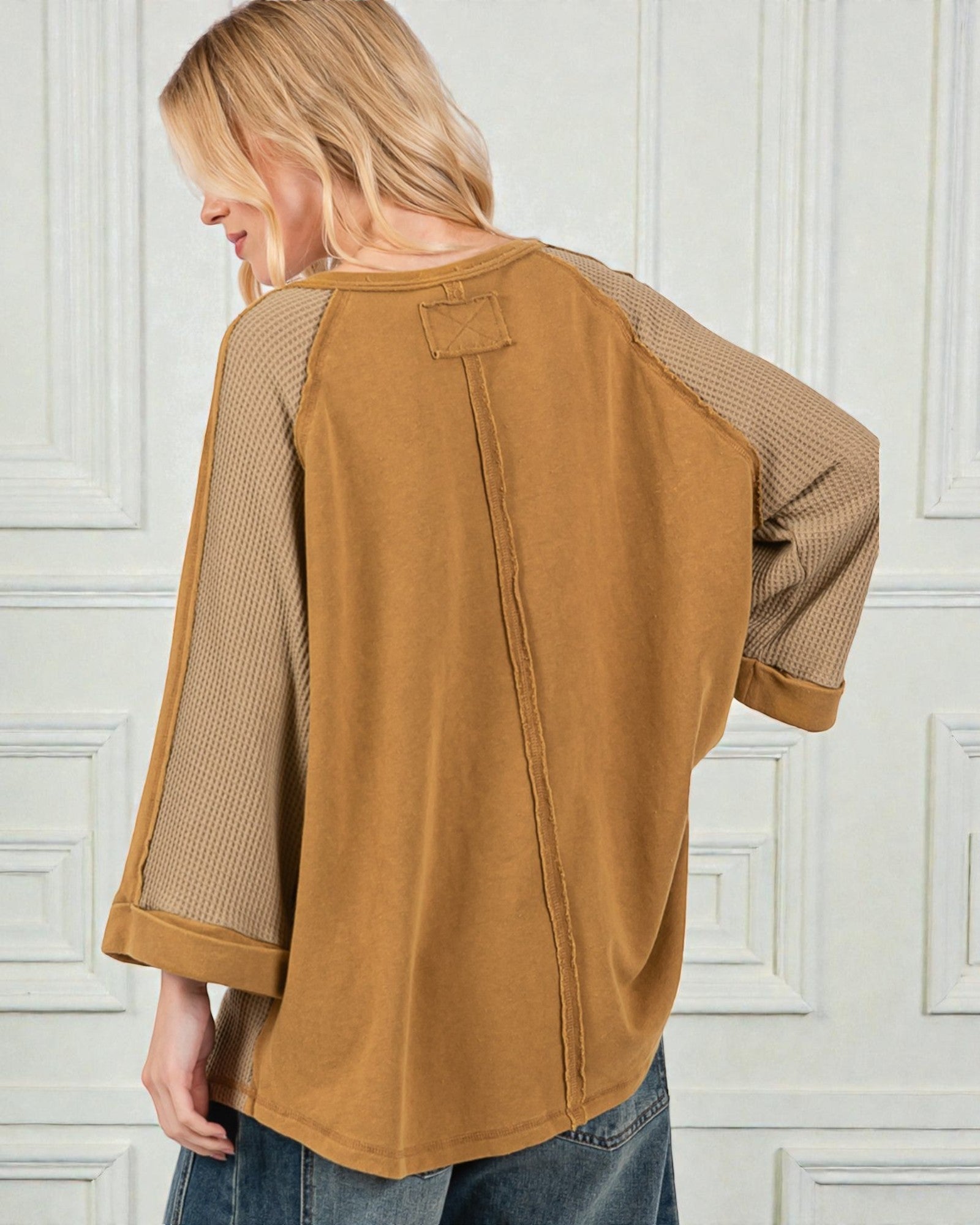 Person wearing a brown shirt with mesh sleeves against a white paneled wall.