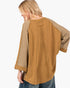 A woman shown from the back wearing a tan and beige long-sleeve top with textured mesh sleeves and a back seam detail, paired with blue jeans against a plain white background.