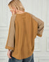 Person wearing a brown shirt with mesh sleeves against a white paneled wall.