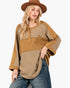 A woman wearing a brown wide-brim hat and a tan and beige patchwork long-sleeve top with a star detail, paired with blue jeans, against a plain white background.