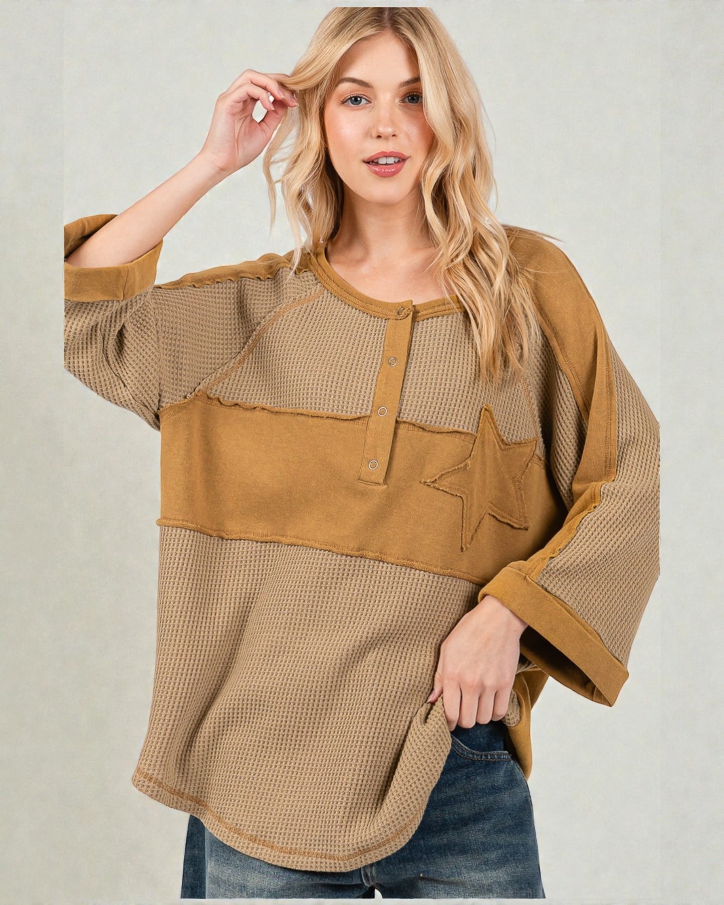 Woman wearing a brown and beige top with a star design on a plain background