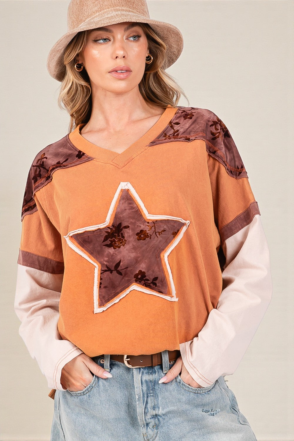 Woman wearing an orange sweater with star design and brown accents, standing against a neutral background.