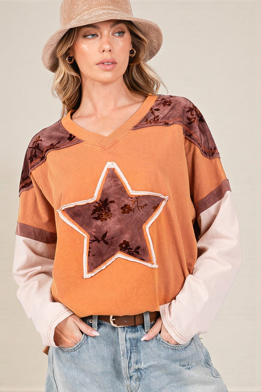 Woman wearing an orange sweater with star design and brown accents, standing against a neutral background.