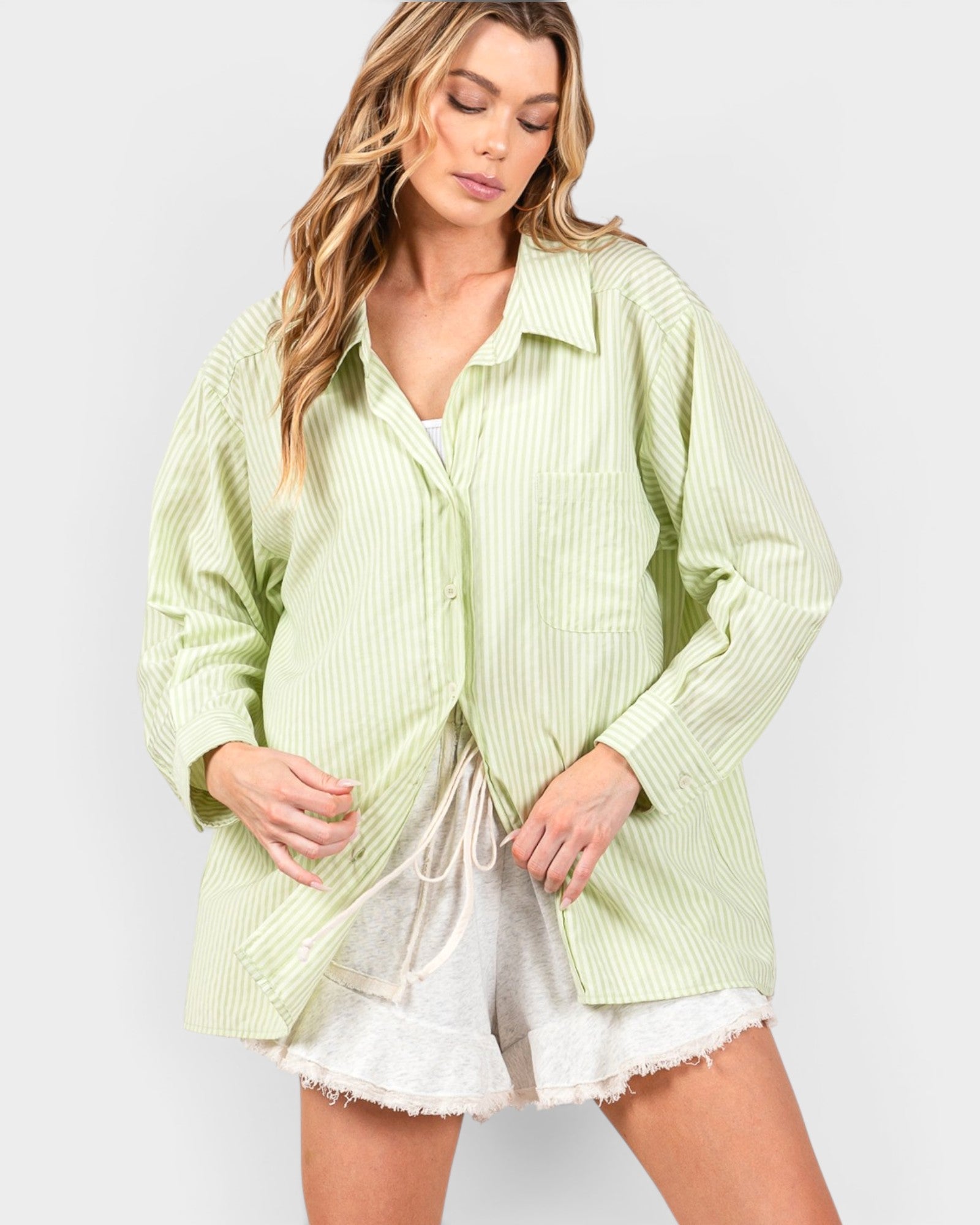 Woman wearing a light green textured shirt over a white top and shorts on a plain background