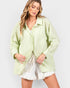 Woman wearing a light green textured shirt over a white top and shorts on a plain background