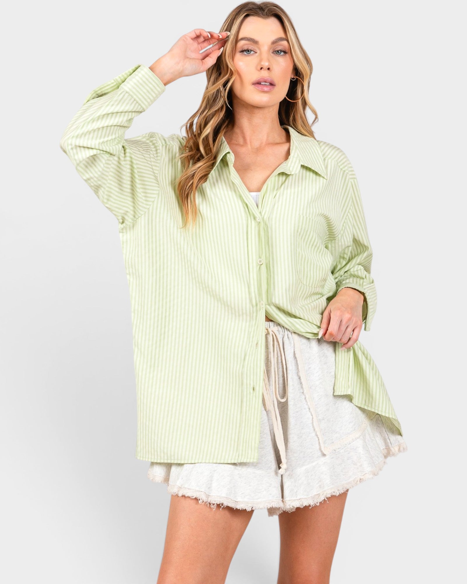 Woman wearing a light green striped shirt and white shorts on a plain background