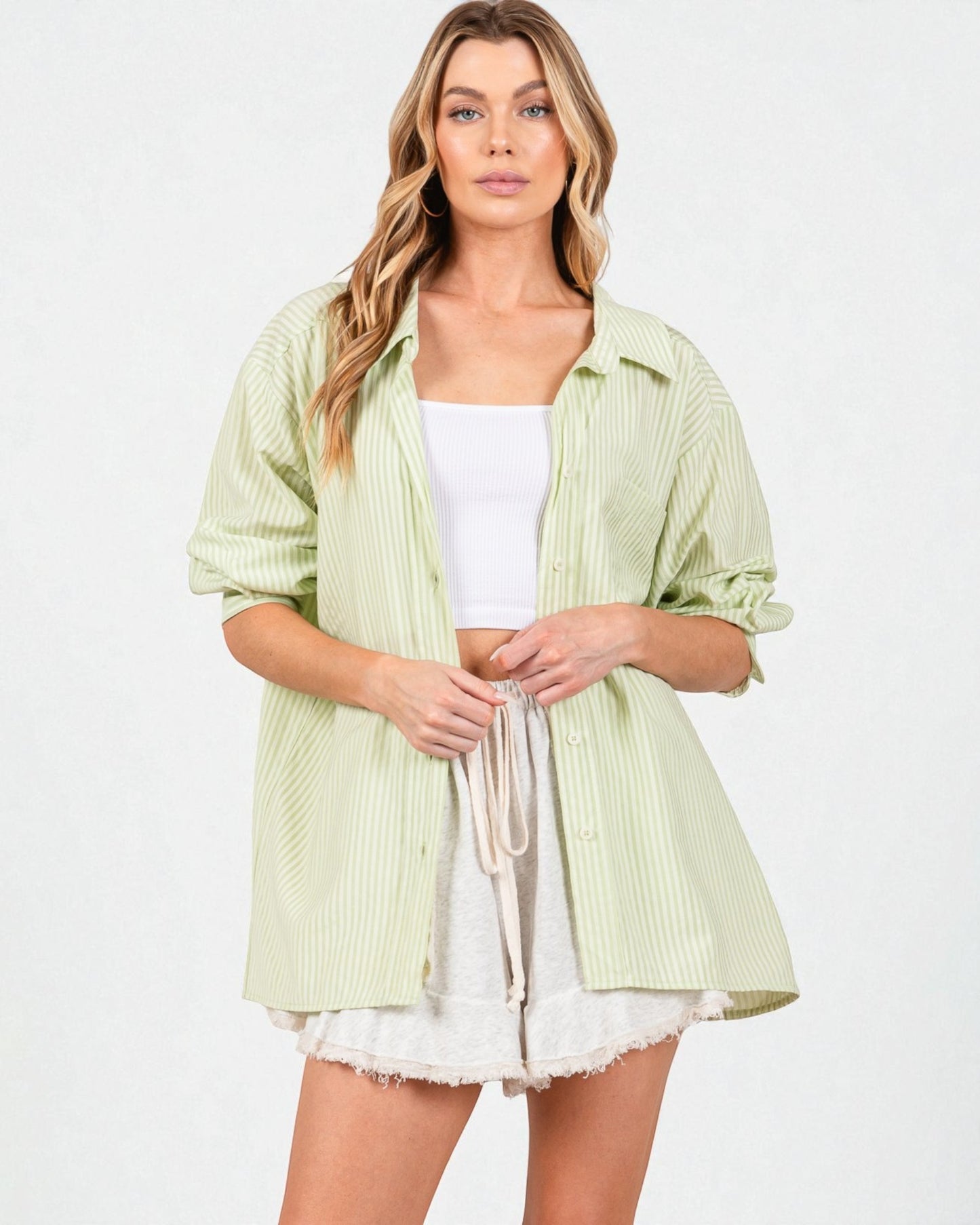 Woman wearing a light green striped shirt over a white top and shorts on a white background