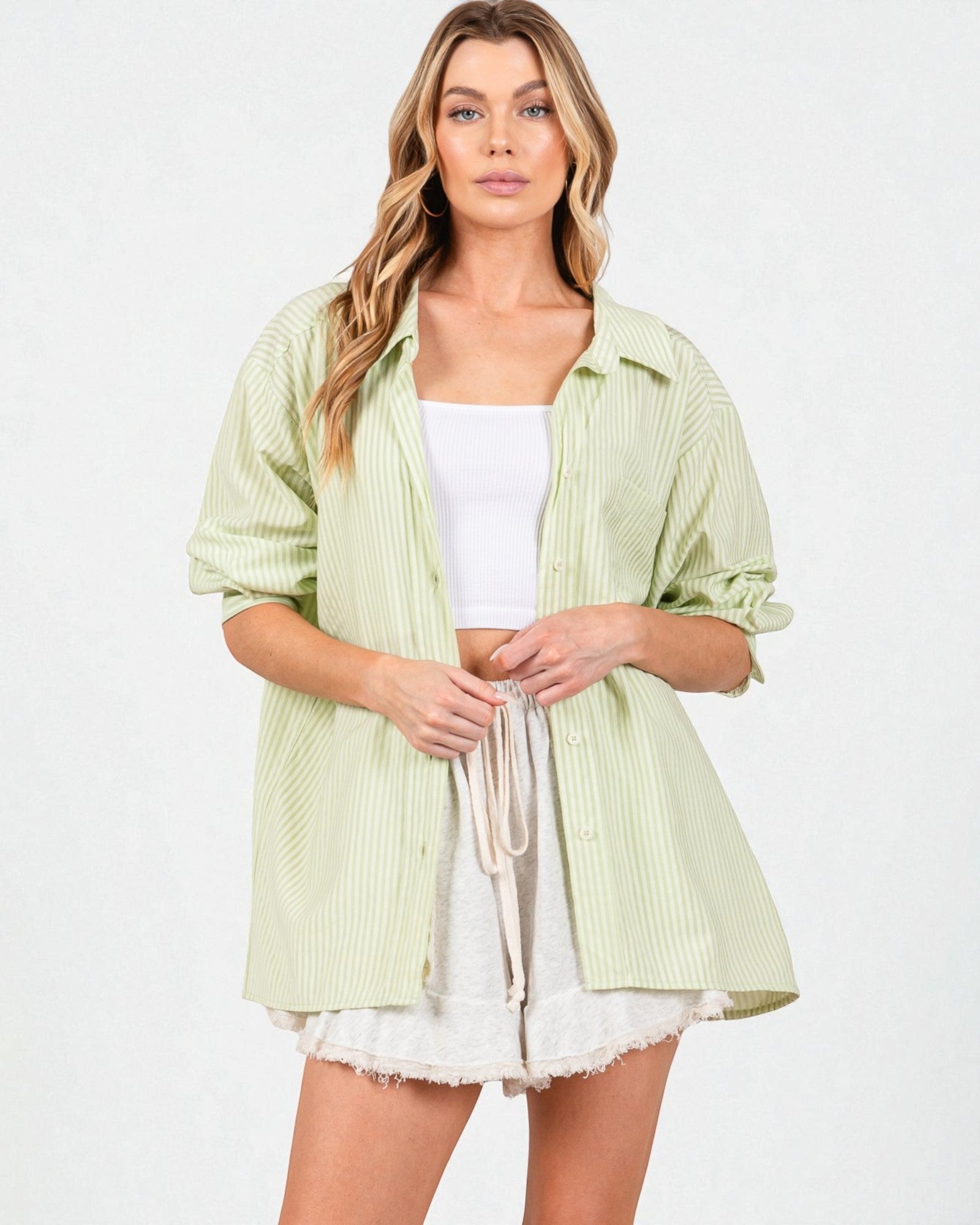 Woman wearing a light green striped shirt over a white top and shorts on a white background