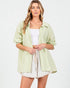 Woman wearing a light green striped shirt over a white top and shorts on a white background
