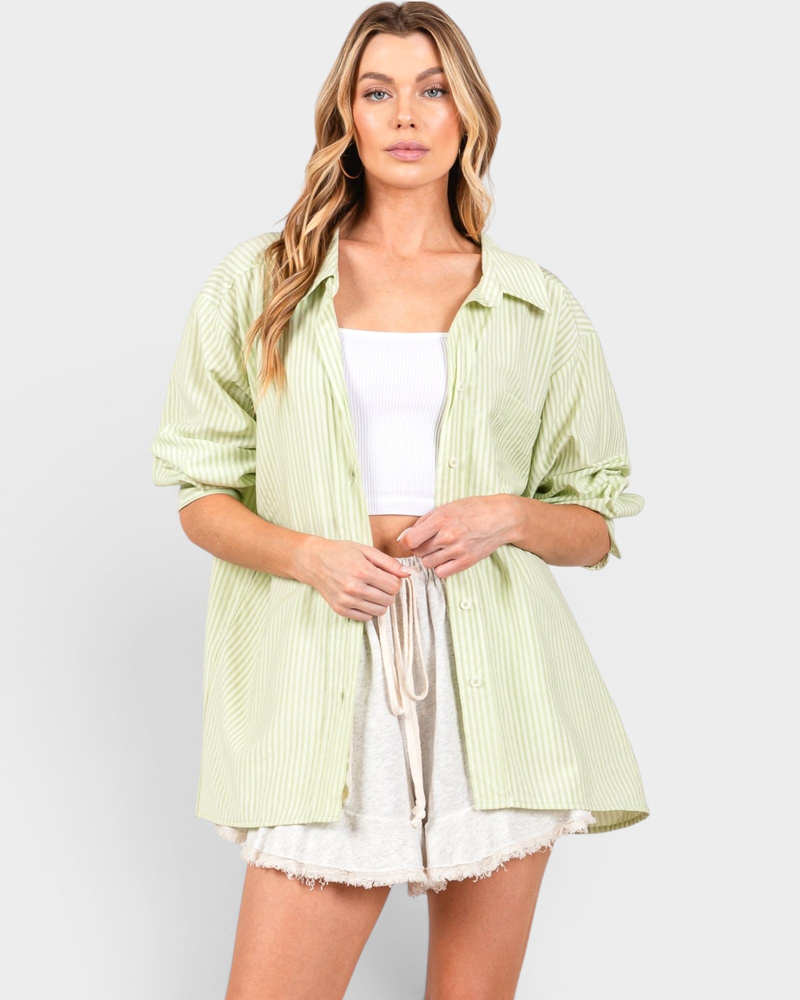 Woman wearing a light green striped shirt over a white top and skirt on a plain background