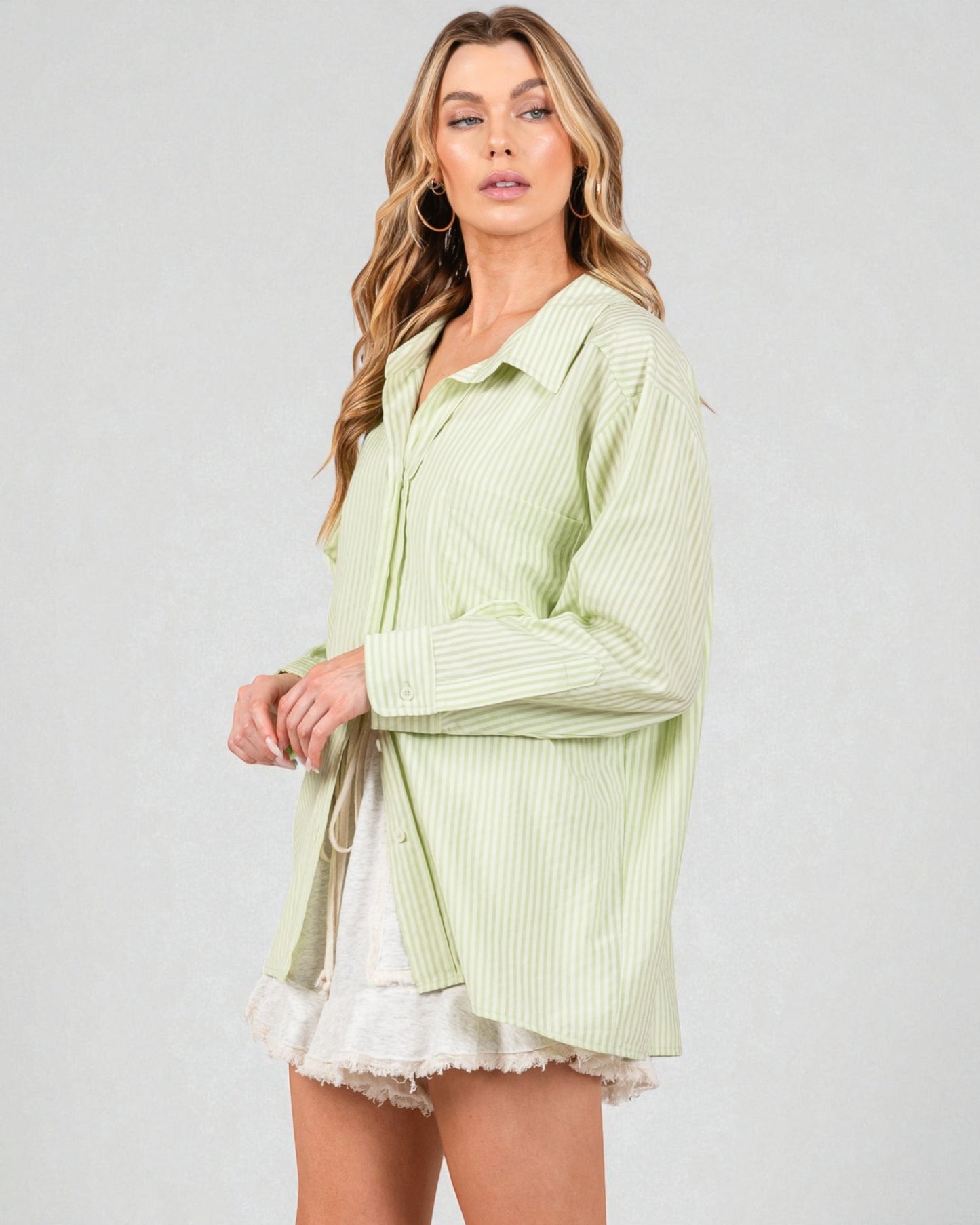 Woman wearing a light green striped shirt over a white top with a gray background