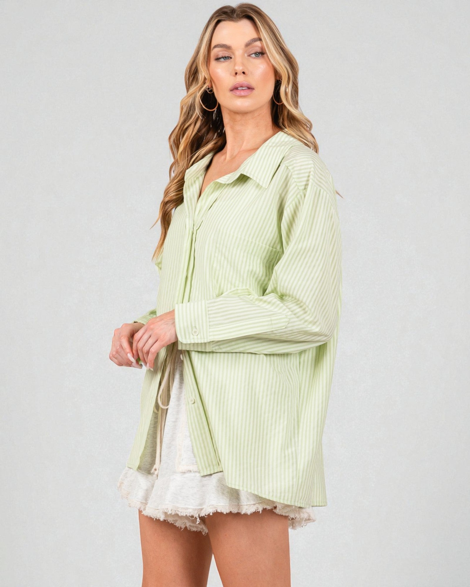 Woman wearing a light green striped shirt over a white top with a gray background